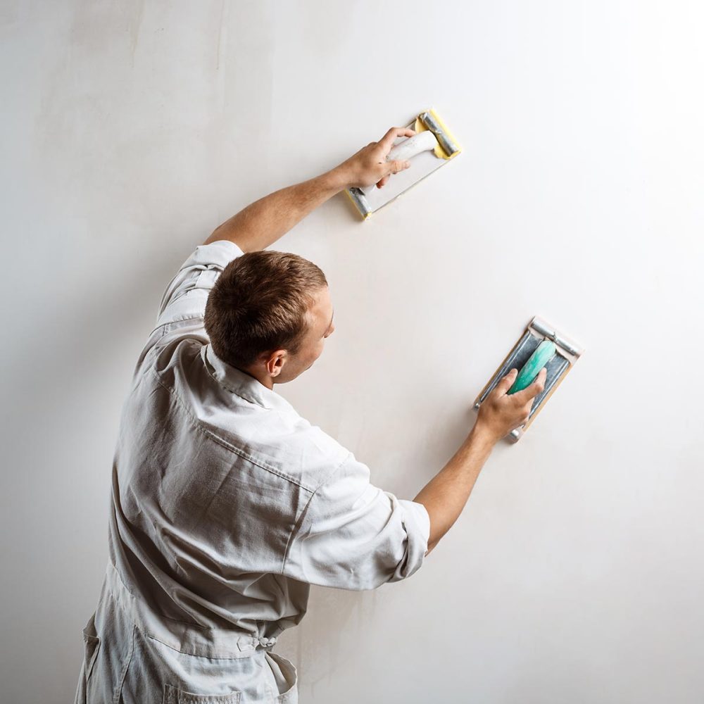 Worker grinding white wall with sandpaper. Copy space.